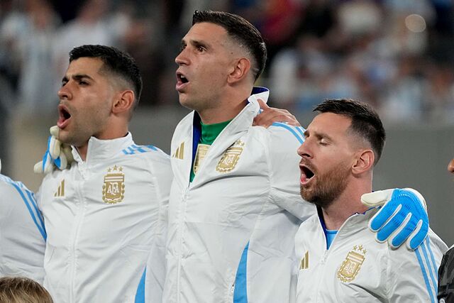 Argentina's Lionel Messi, right, and Cristian Romero flank goalkeeper Emiliano Martinez while singing the national anthem prior to a Copa America match